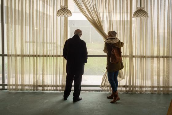 Deux personnes soulèvent un rideau et regardent la cour de la caserne Lourcine